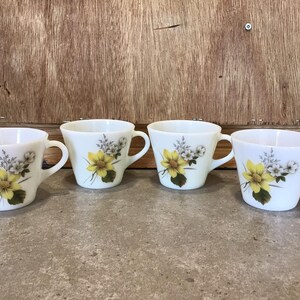 Pode incluir: Conjunto de quatro ch&aacute;venas de ch&aacute; de cer&acirc;mica branca com um design floral com flores amarelas e brancas. As ch&aacute;venas t&ecirc;m uma forma arredondada e uma pega no lado.