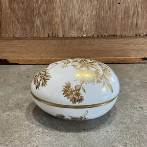 May include: White ceramic egg-shaped trinket box with a gold floral design.