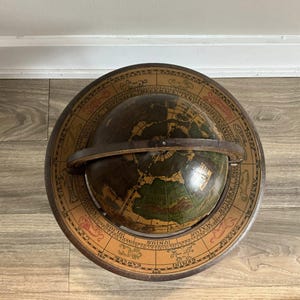May include: An antique globe with a dark brown sphere depicting continents in green and brown. The globe is set within a circular frame with zodiac symbols and months. A leather band secures the globe.