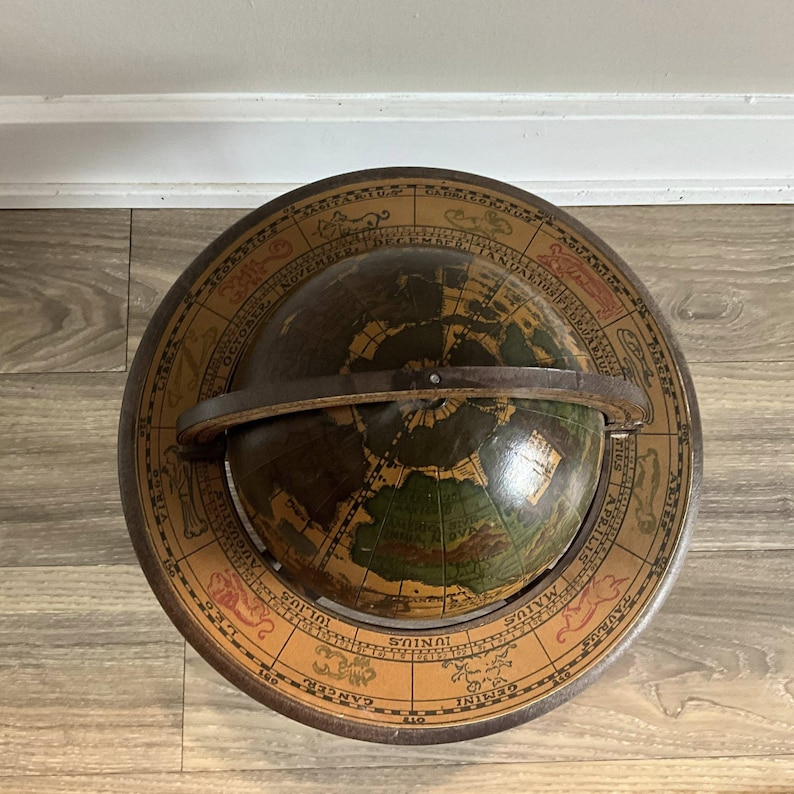 May include: An antique globe with a dark brown sphere depicting continents in green and brown. The globe is set within a circular frame with zodiac symbols and months. A leather band secures the globe.