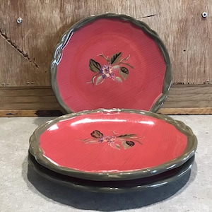 May include: Three pink ceramic dinner plates with a green rim and a floral design. The plates are stacked on top of each other.