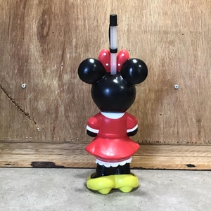 May include: A Minnie Mouse-shaped tumbler with a red dress, white trim, and yellow shoes. The black head features large ears and a red bow with white polka dots. A black and white straw extends from the top.