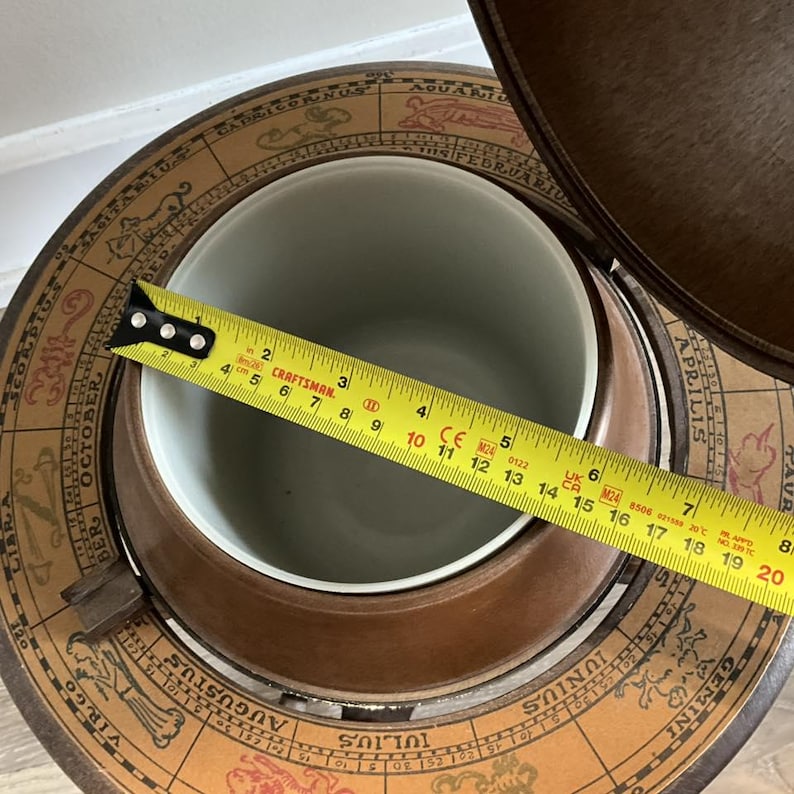 May include: A vintage globe-shaped bar with a light brown wooden exterior. The interior is a light green color. The opening of the interior measures approximately 7 inches in diameter. The globe is decorated with zodiac signs.