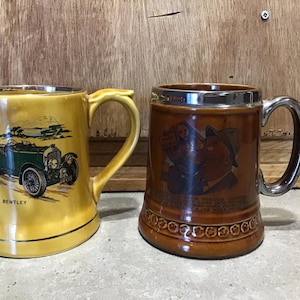 Puede incluir: Dos tazas de cerámica. Una taza es marrón con un borde plateado y presenta una ilustración de dibujos animados de un hombre con bigote. La otra taza es amarilla con un borde plateado y presenta un coche antiguo verde con la palabra "BENTLEY" impresa en el lateral.