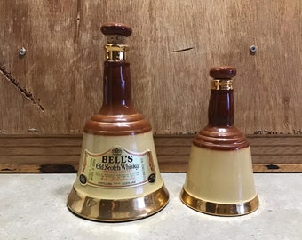 Puede incluir: Dos decantadores de cerámica Bell's Old Scotch Whisky con forma de campana. El decantador más grande tiene un borde dorado y la etiqueta dice "Bell's Old Scotch Whisky Special Selected" y "Distillers Scotland".