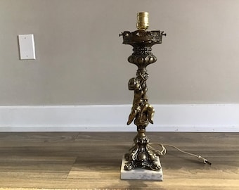 May include: A gold-toned table lamp with a cherub figure holding onto the lamp post. The lamp has a white marble base.
