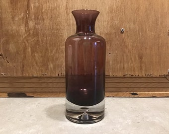 May include: A dark brown glass vase with a clear glass base. The vase has a rounded bottom and a narrow neck.