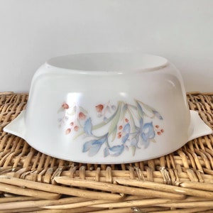 Könnte beinhalten: Weiße Keramik-Backform mit einem Blumendesign mit blauen und rosa Blüten und grünen Blättern.