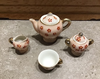 May include: A miniature tea set with a teapot, creamer, sugar bowl, and cup. The set is decorated with a floral pattern in shades of pink and red.