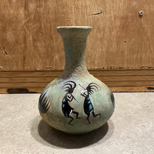 Pode incluir: Um vaso de cerâmica verde com corpo redondo e pescoço estreito. O vaso é decorado com um desenho pintado de duas figuras em preto, azul e amarelo.