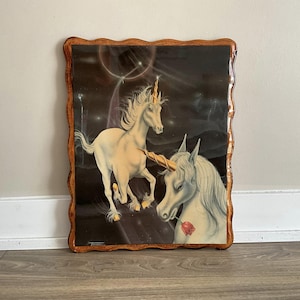Puede incluir: Una impresión enmarcada de dos unicornios blancos con cuernos dorados sobre un fondo oscuro con estrellas y una rosa roja. El marco es de madera con un borde ondulado.