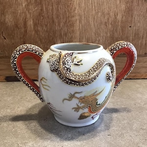 Op de afbeelding: Witte keramische roomkan met rood en gouden drakenontwerp en rode handvatten.