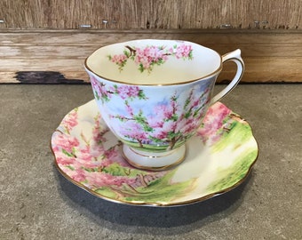 May include: A vintage teacup and saucer set with a floral design featuring pink blossoms and green leaves. The set is decorated with a gold trim.