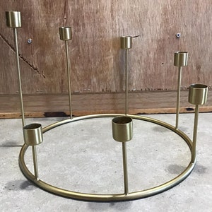 May include: A gold metal candle holder with a circular base and seven candle holders. The candle holder is on a grey surface.
