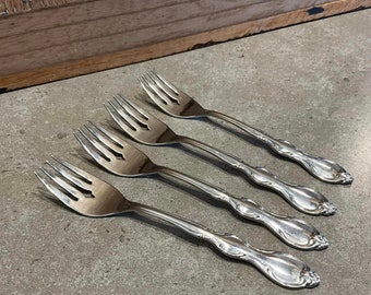 Peut inclure: Quatre fourchettes en argent avec des manches ornés. Les fourchettes sont disposées en rangée, les manches pointant vers la droite.