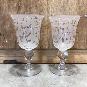 Puede incluir: Dos copas de vidrio esmerilado con un delicado diseño floral grabado. Las copas tienen un tallo y una base de vidrio transparente.