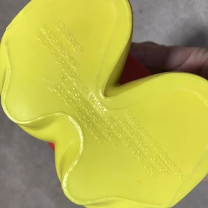 May include: A yellow plastic Disney character foot with red accents. The underside of the foot has embossed text that reads "&copy;DISNEY MADE IN CHINA WASH THOROUGHLY IN WARM WATER BEFORE USE NOT DISHWASHER SAFE DO NOT MICROWAVE".