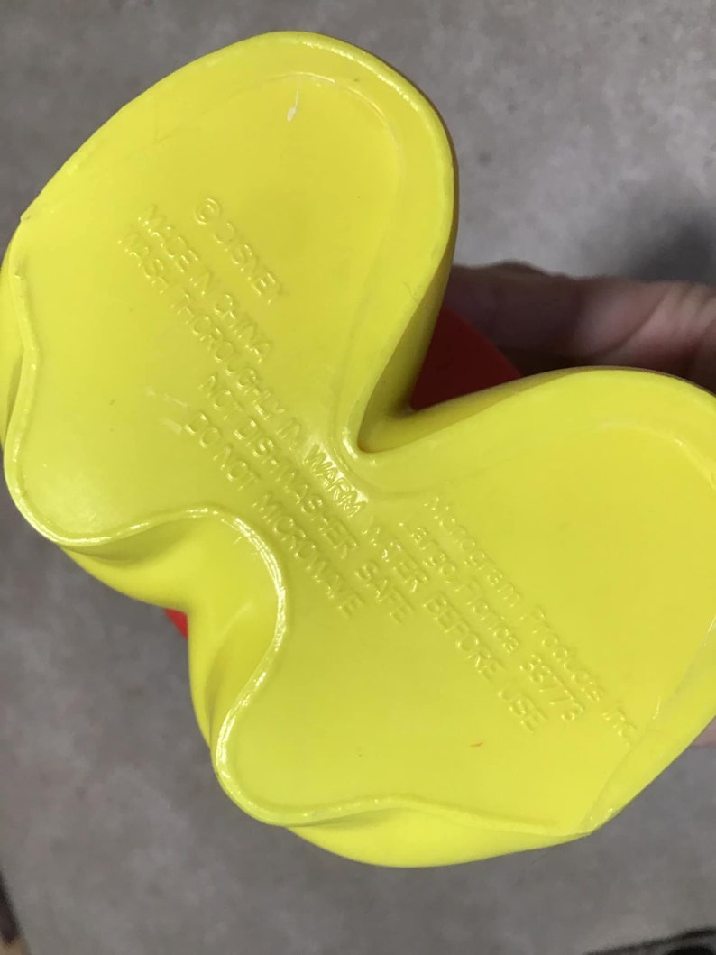 May include: A yellow plastic Disney character foot with red accents. The underside of the foot has embossed text that reads "&copy;DISNEY MADE IN CHINA WASH THOROUGHLY IN WARM WATER BEFORE USE NOT DISHWASHER SAFE DO NOT MICROWAVE".