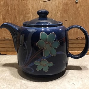 May include: A blue ceramic teapot with a floral design. The teapot has a lid and a handle. The flowers are green and blue.