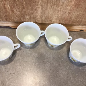 Pode incluir: Quatro ch&aacute;venas de ch&aacute; de cer&acirc;mica branca com um design floral. As ch&aacute;venas est&atilde;o vazias e t&ecirc;m um fundo branco com acentos florais amarelos e verdes.