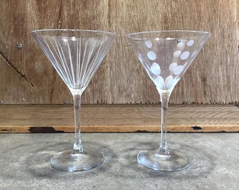 Op de afbeelding: Twee heldere glazen martini glazen met gegraveerde ontwerpen. Een glas heeft een zonnestralenpatroon en het andere heeft een stippenpatroon.