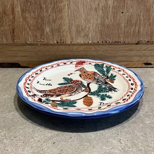 Może przedstawiać: Owalny ceramiczny talerz z niebieską obw&oacute;dką i dekoracyjną bordiurą z czerwonych i białych kropek. Talerz przedstawia dwa ptaki siedzące na gałęzi z igłami sosnowymi i szyszką. Na talerzu widnieje napis "Two Turtle".