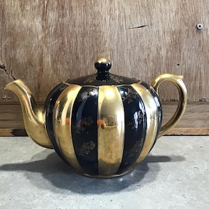 May include: A vintage teapot with a black and gold striped design. The teapot features a gold handle, spout, and lid. The black stripes are adorned with small gold floral patterns, creating an elegant and classic look. The teapot is a decorative item.