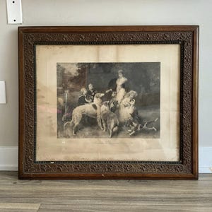 Op de afbeelding: Een antieke ingelijste prent met een zwart-wit illustratie van mensen en honden. De prent zit in een donkerhouten lijst met sierlijke details. De afbeelding toont een historische scène.