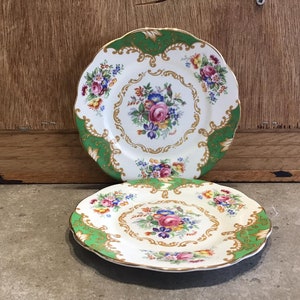 May include: Two white porcelain plates with a green and gold floral design. The plates have a scalloped edge and a raised centre design.