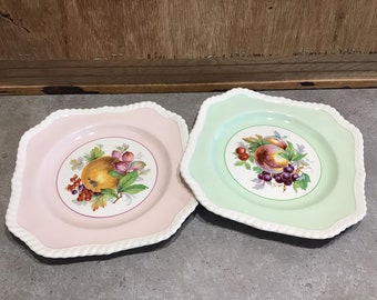 Puede incluir: Dos platos cuadrados de cerámica con un borde de diseño de cuerda blanca. Los platos presentan un motivo de fruta con fondo rosa y verde.