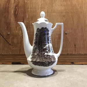 May include: White ceramic coffee pot with a brown and black woodland scene design. The pot has a lid and a handle.