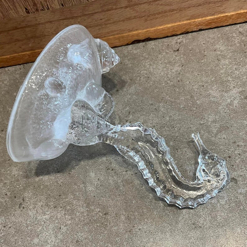 May include: A clear glass seahorse figurine with a textured surface. The seahorse is curled in a decorative pose.