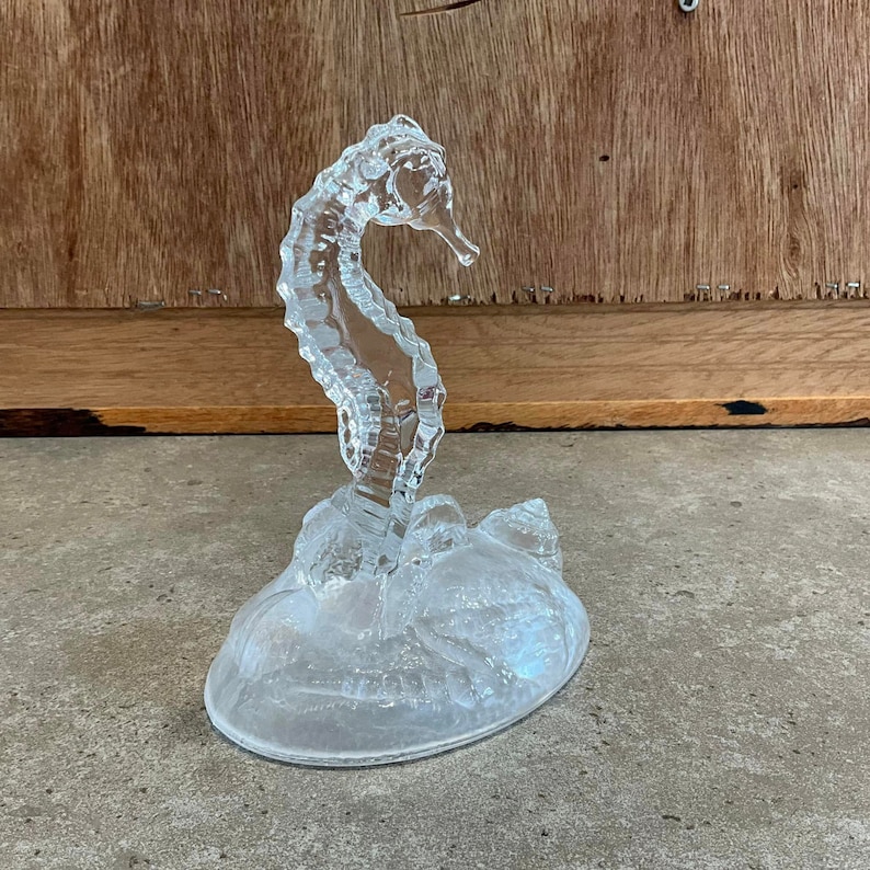 May include: A clear glass sculpture of a seahorse on a base of swirling glass waves.