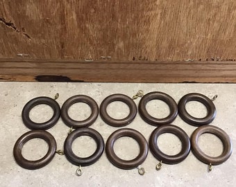Könnte beinhalten: Zehn braune Holz-Vorhangringe mit goldenen Metallhaken. Die Ringe sind in zwei Reihen zu fünf angeordnet.