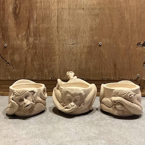 Può includere: Tre vasi in terracotta a forma di scimmia, ognuno con un'espressione diversa. La scimmia a sinistra guarda di lato, la scimmia al centro guarda dritto, e la scimmia a destra si copre gli occhi con le mani.