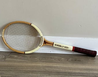 Könnte beinhalten: Ein Vintage-Slazenger-Tennisschläger mit Holzrahmen und weißem Griff. Der Schläger hat einen cremefarbenen Kopf und einen braunen Griff mit einem dunkelroten Griff. Die Saiten sind weiß.