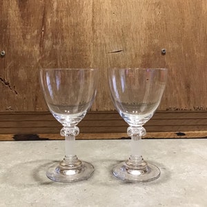 May include: Two clear glass wine glasses with a fluted bowl and a column-shaped stem. The glasses have a frosted finish on the stem.