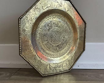 Puede incluir: Bandeja octogonal de latón con un intrincado diseño en relieve. El centro presenta un motivo circular con un símbolo chino. La bandeja tiene un borde con cuentas.