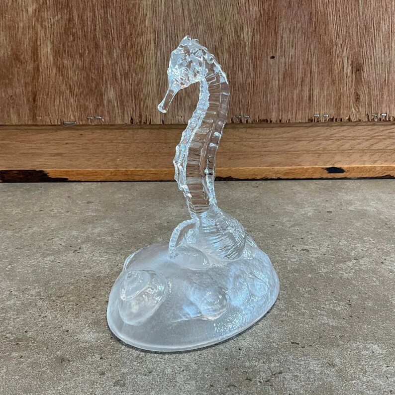 May include: A clear glass sculpture of a seahorse on a base with a textured surface.