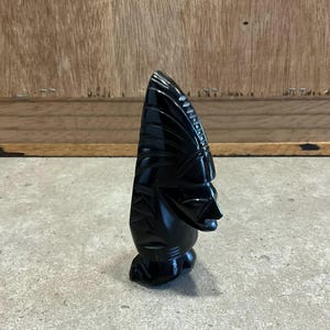 Pode incluir: Uma escultura de obsidiana preta de uma cabeça humana com um chapéu. A escultura é esculpida com detalhes intrincados e tem um acabamento liso e polido.