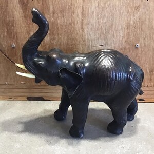 Puede incluir: Una figurita de elefante de madera tallada en color negro con la trompa levantada en el aire. El elefante tiene colmillos de color marfil.