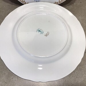 May include: White ceramic plate with a scalloped edge. The back of the plate has a green and gold mark that reads "Made in England".