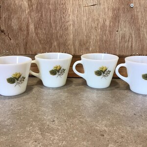 Pode incluir: Quatro ch&aacute;venas de ch&aacute; de cer&acirc;mica branca com um design floral com flores amarelas e folhas verdes.
