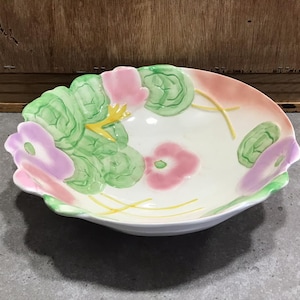 Op de afbeelding: Een witte keramische kom met een gegolfde rand en een bloemenontwerp. De kom heeft roze, groene en gele bloemen.