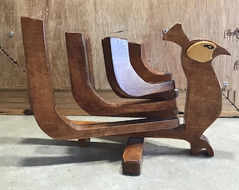 May include: A wooden peacock-shaped stand with four tiers. The stand is made of dark brown wood and has a light brown eye detail.