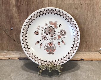 Może przedstawiać: Biały ceramiczny talerz obiadowy z brązowym i różowym wzorem kwiatowym. Talerz ma falisty brzeg i brązową obwódkę z powtarzającym się wzorem małych serc.