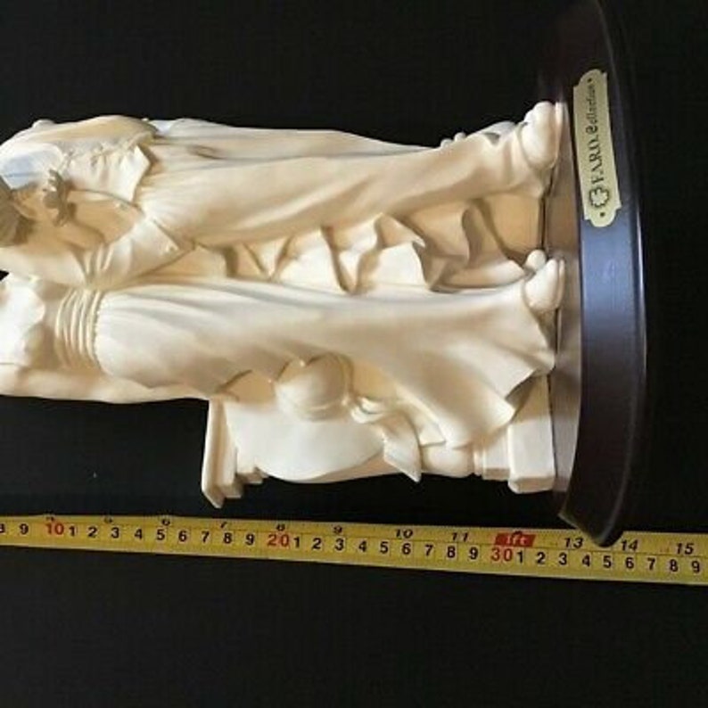 May include: A white porcelain figurine of two figures embracing. The figurine is mounted on a dark wood base with a gold plaque that reads "FARO Editions".