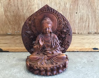 May include: A detailed wooden Buddha statue in a seated meditation pose. The statue is a warm brown color and features intricate carvings, including a lotus flower base and a decorative halo. The Buddha is depicted with a serene expression.