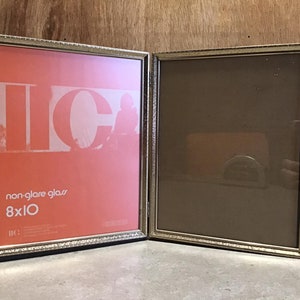 May include: A silver picture frame with a decorative border. The frame is 8x10 inches and has a non-glare glass. The frame is empty on the right side and has a red background with the letters "IC" on the left side.