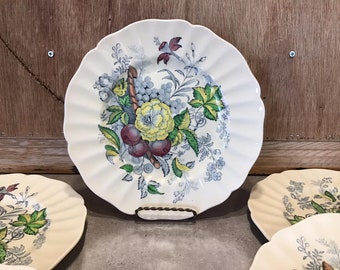 Puede incluir: Juego de cuatro platos de cena de cerámica blanca con un patrón floral que presenta hojas verdes, flores amarillas y frutas moradas y rojas. Los platos tienen un borde festoneado.